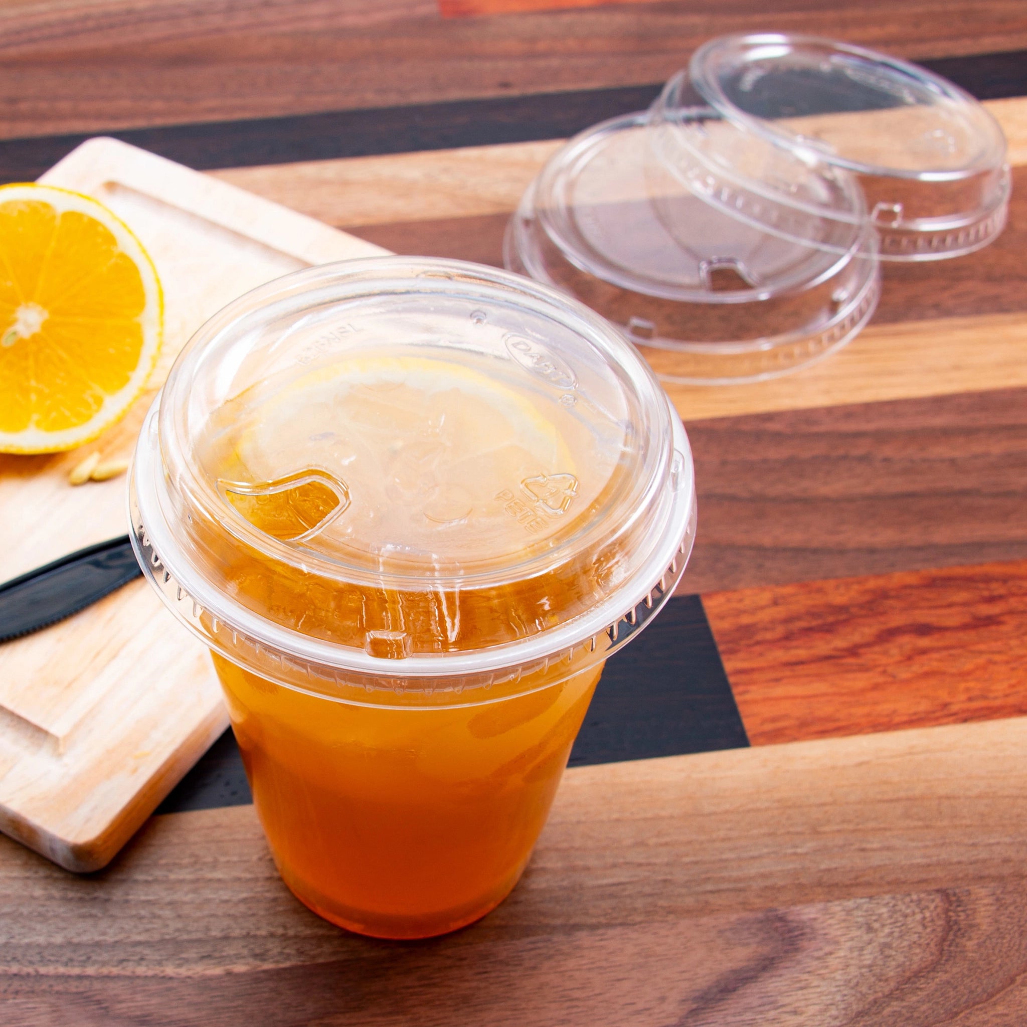 Dart 626NSL sip‑through lid sealing a 16 oz PET cup filled with orange juice; two extra 98 mm lids displayed in background.