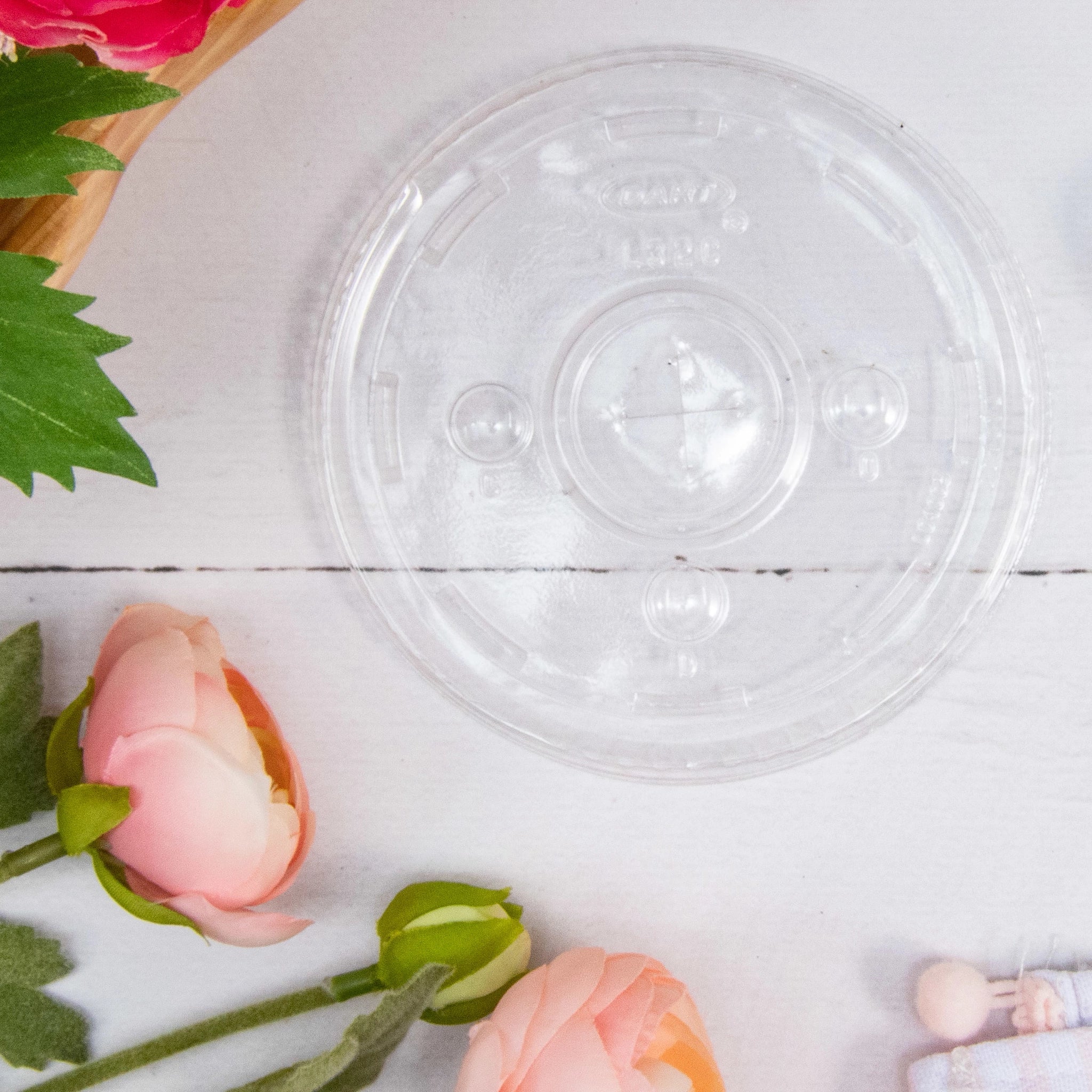 DART L32CR clear flat lid for DART 32AC plastic cups on white wood surface with pink flowers